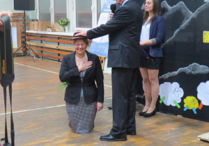 Dyrektor szkoły Barbara Makowska na kolanach przyjmuje kapelusz góralski od Kazimierza Tischnera
